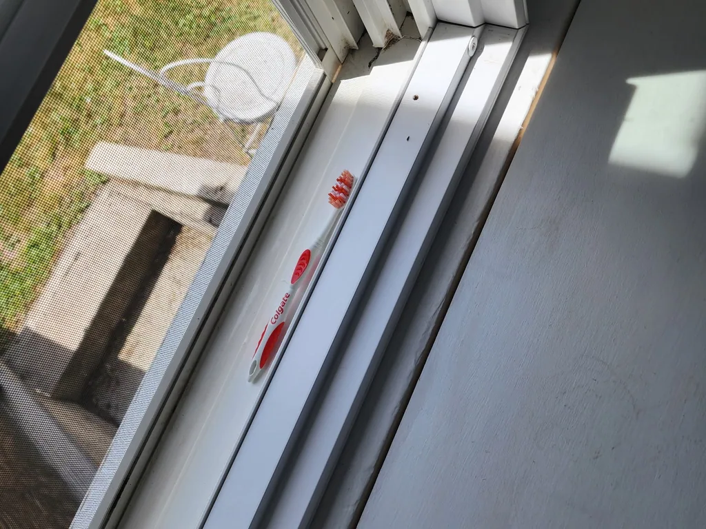 The same window sill and track cleaned out to bare white, with the detailing brush resting on the sill.